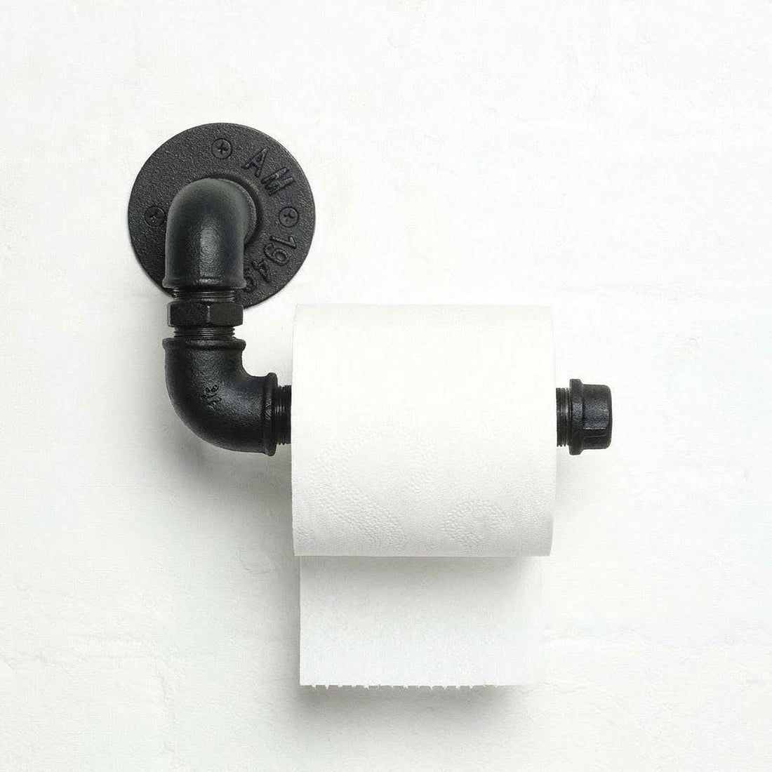 A black pipe-style toilet paper holder with a roll of white toilet paper attached to it, mounted on a white wall.