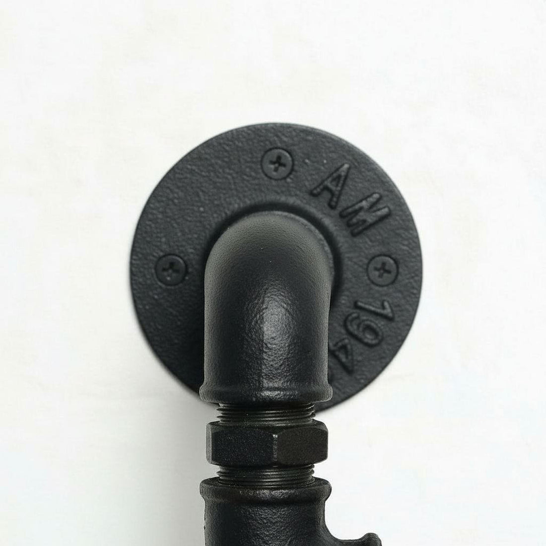 A close-up view of a black pipe or pipe fitting mounted on a wall, with the pipe&