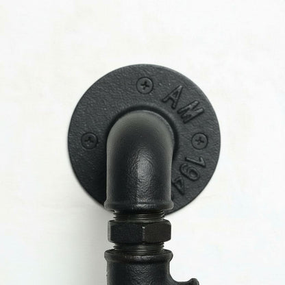 A close-up view of a black pipe or pipe fitting mounted on a wall, with the pipe&