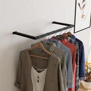 wall-mounted clothing rack with wooden hangers holding shirts and jackets, placed against a neutral wall with minimal decor.