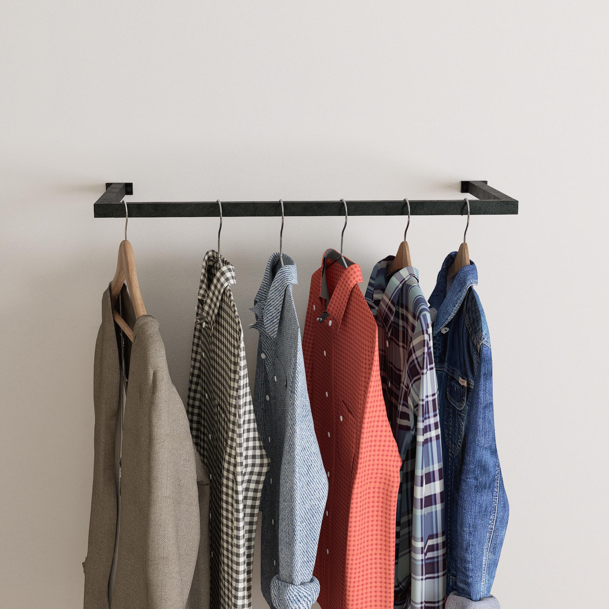 wall-mounted clothing rack with wooden hangers holding shirts and jackets, placed against a neutral wall with minimal decor.