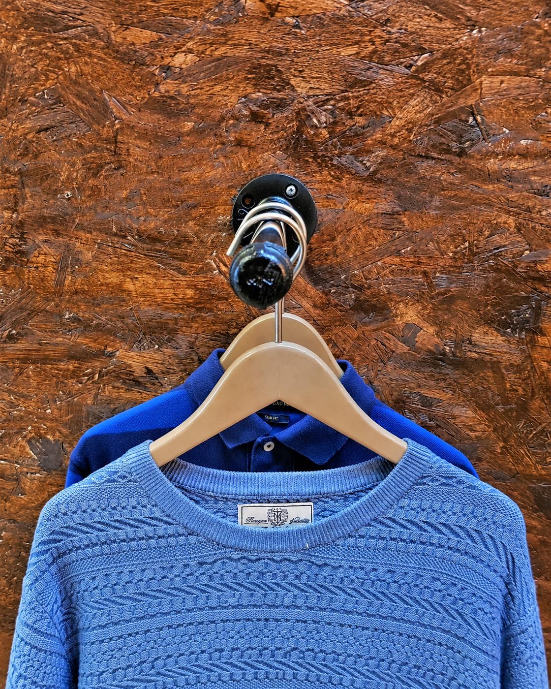 Front view of the Flux wall-mounted pipe clothes rail holding a blue jumper and shirt on wooden hangers.